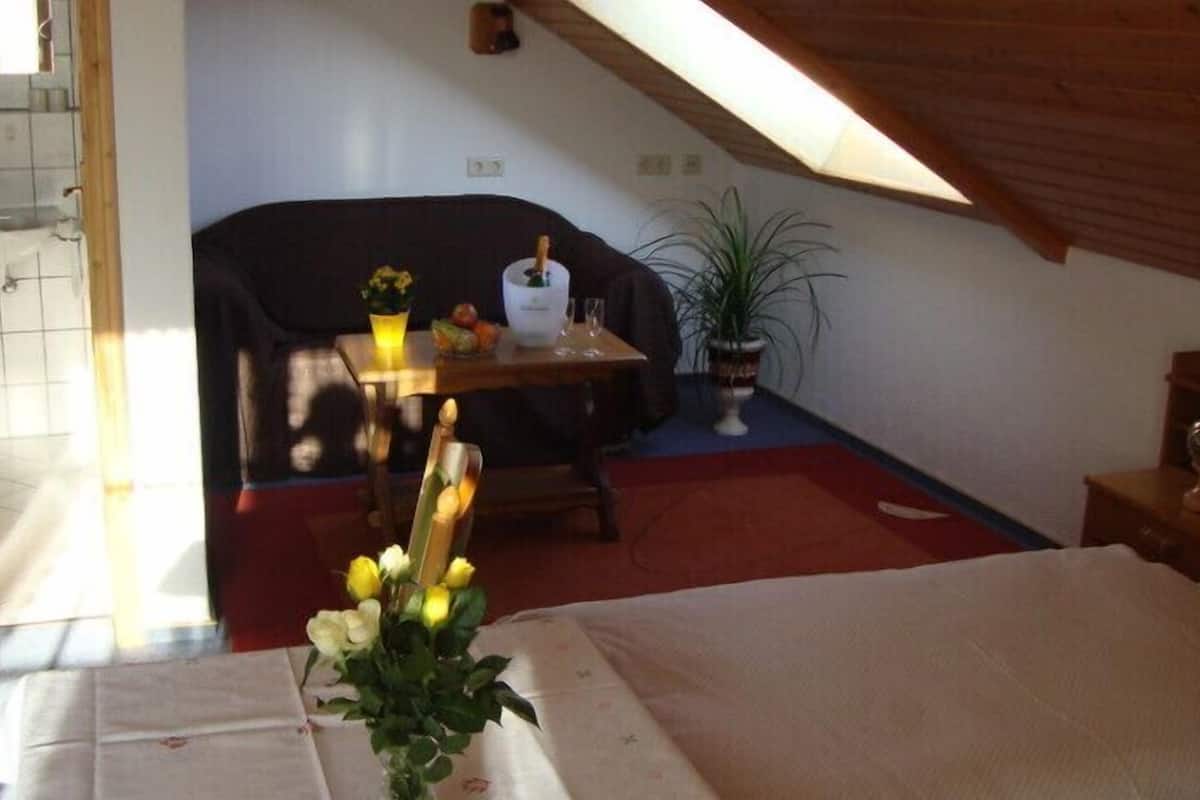 Een knus kamertje met een bed, een tafel met een bloevas, een stoel en een potplant.