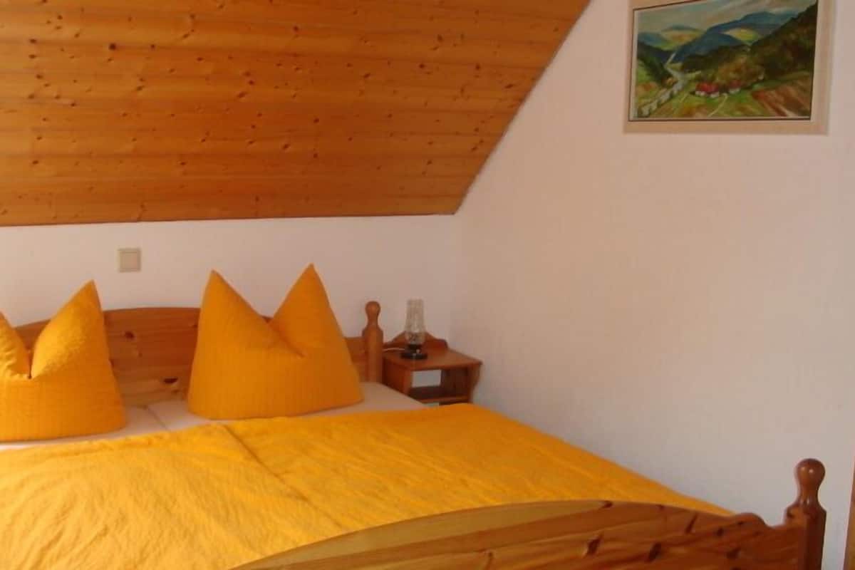 Een slaapkamer met een houten plafond, een bed met geel beddengoed en een nachtkastje met een lamp.