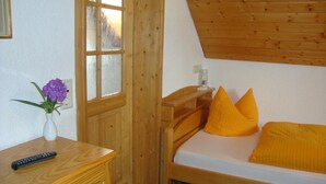 Un letto di legno con due cuscini, un comodino con un telecomando e un vaso con fiori viola.