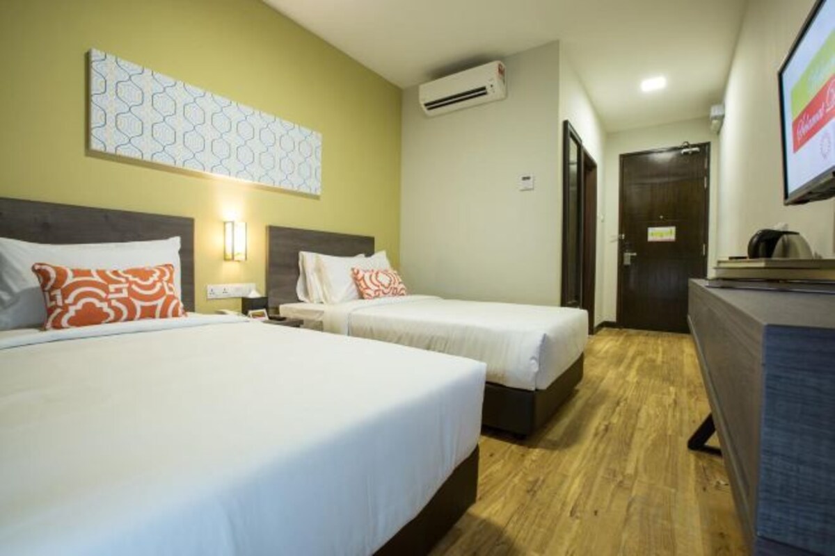 A hotel room with two beds, a desk, a TV, and an air conditioning unit.