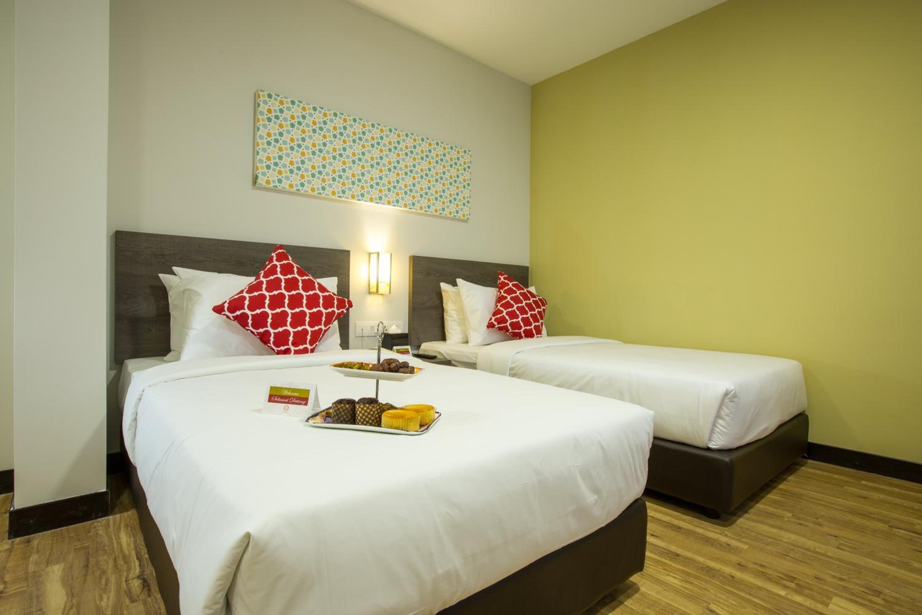 Habitación de hotel con dos camas, un adorno en la pared y una bandeja de pasteles sobre la cama.