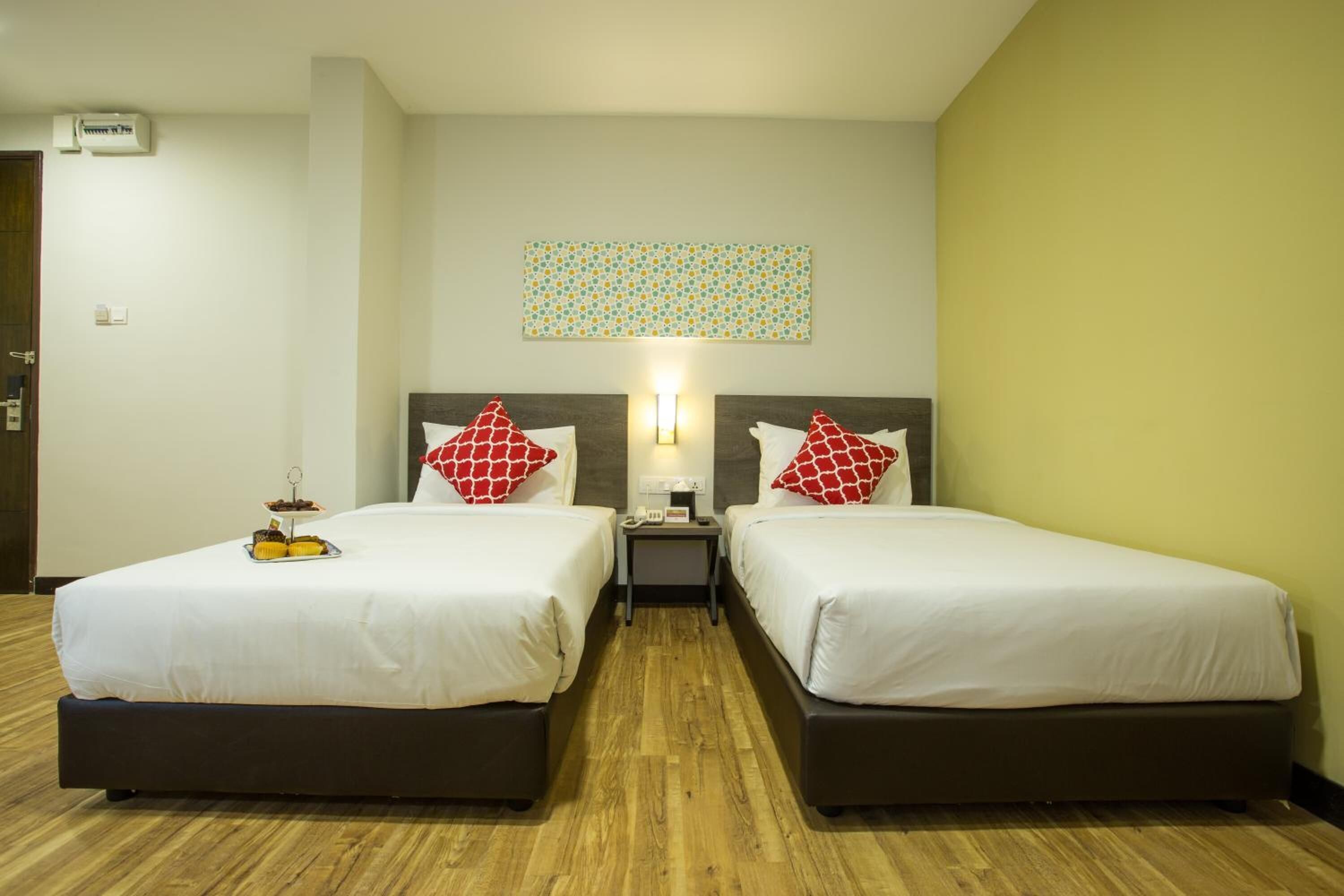 Une chambre d’hôtel avec deux lits, une table de chevet, une lampe fixée au mur et une petite table sur laquelle se trouve un plateau de collations.