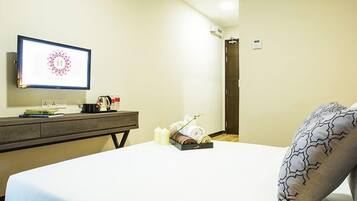A hotel room with a bed, a bedside table with a vase of flowers, a flat-screen TV, and a wall-mounted air conditioning unit.