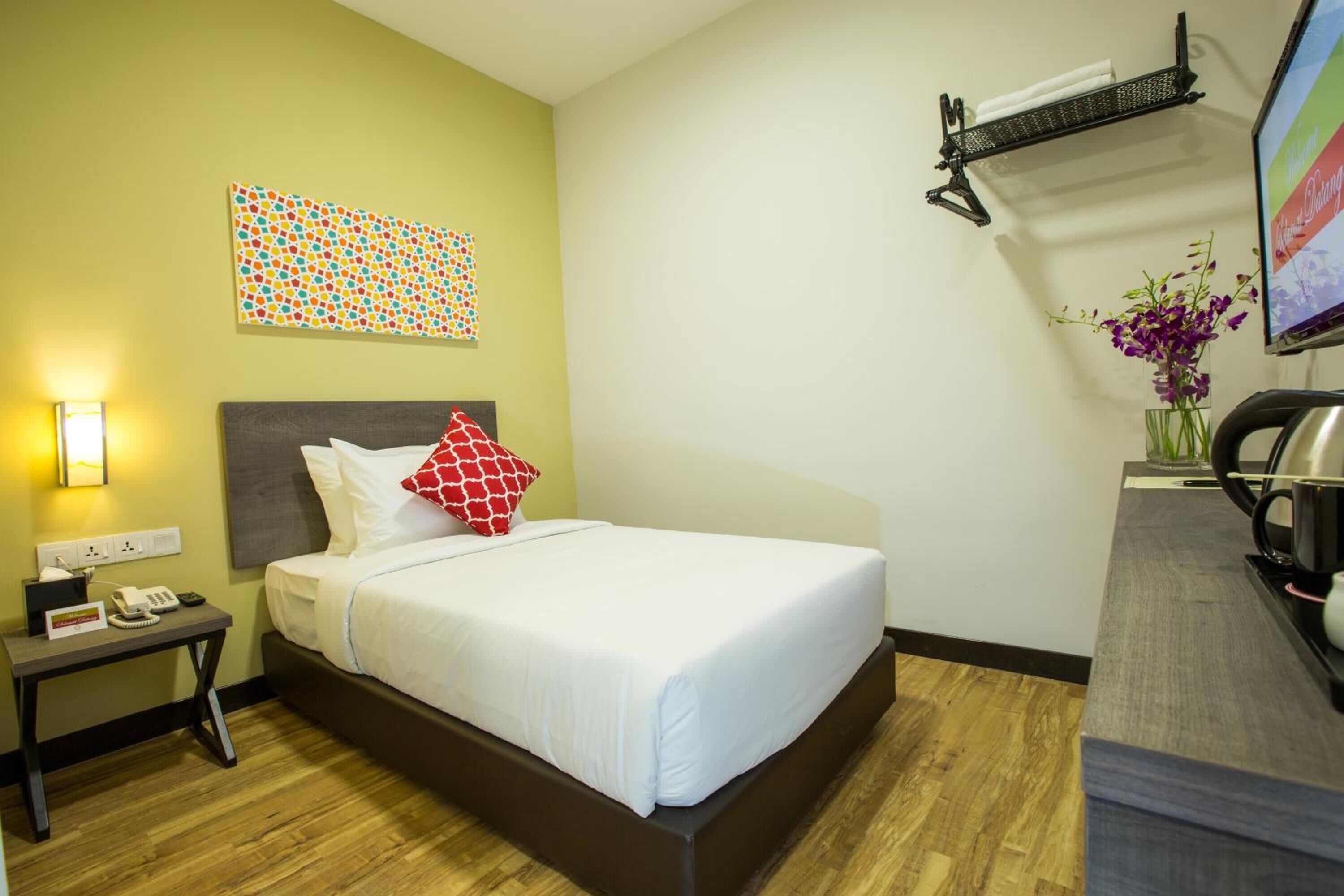 Una habitación de hotel con cama, mesita de noche, lámpara y televisor montado en la pared.