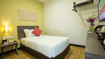 Una habitación de hotel con cama, mesita de noche, lámpara y televisor montado en la pared.