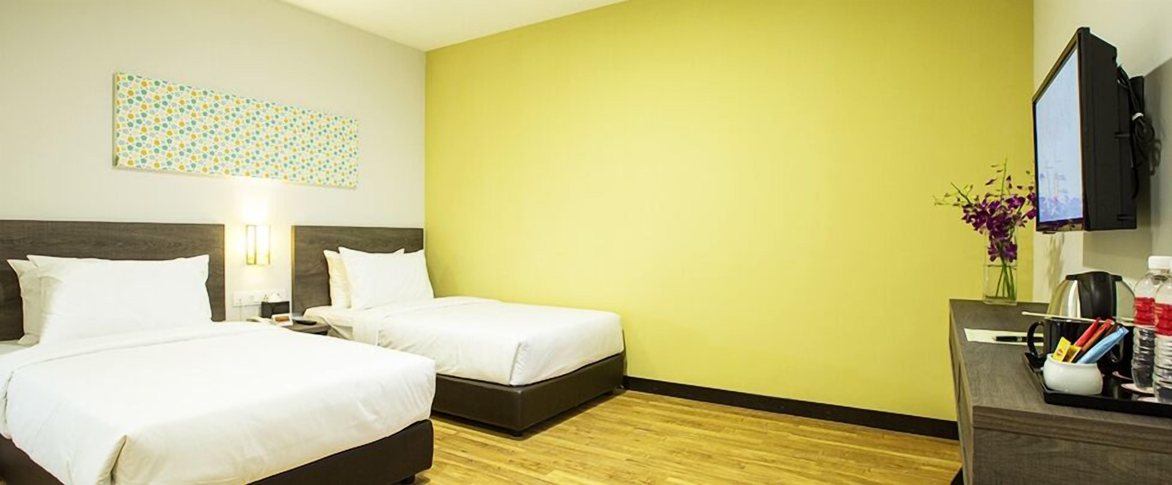 A hotel room with two beds, a desk with a flat-screen TV, a vase with flowers, and a wall art piece.