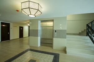 A spacious lobby with a modern elevator, a staircase, and a decorative light fixture.