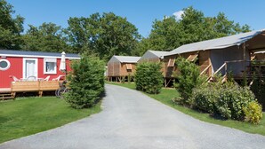 A row of cabins with a gravel path leading to them, surrounded by greenery and trees. - Camping Les Chèvrefeuilles (Royan)