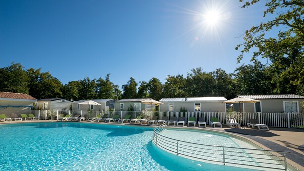 A clear swimming pool with lounge chairs and umbrellas, surrounded by mobile homes. - Camping Les Chèvrefeuilles (Royan)