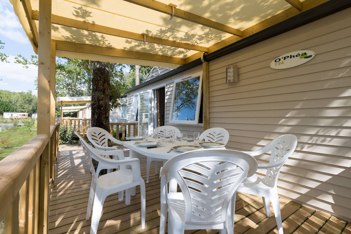 A covered outdoor patio with a wooden deck, white plastic chairs, and a table set for dining.