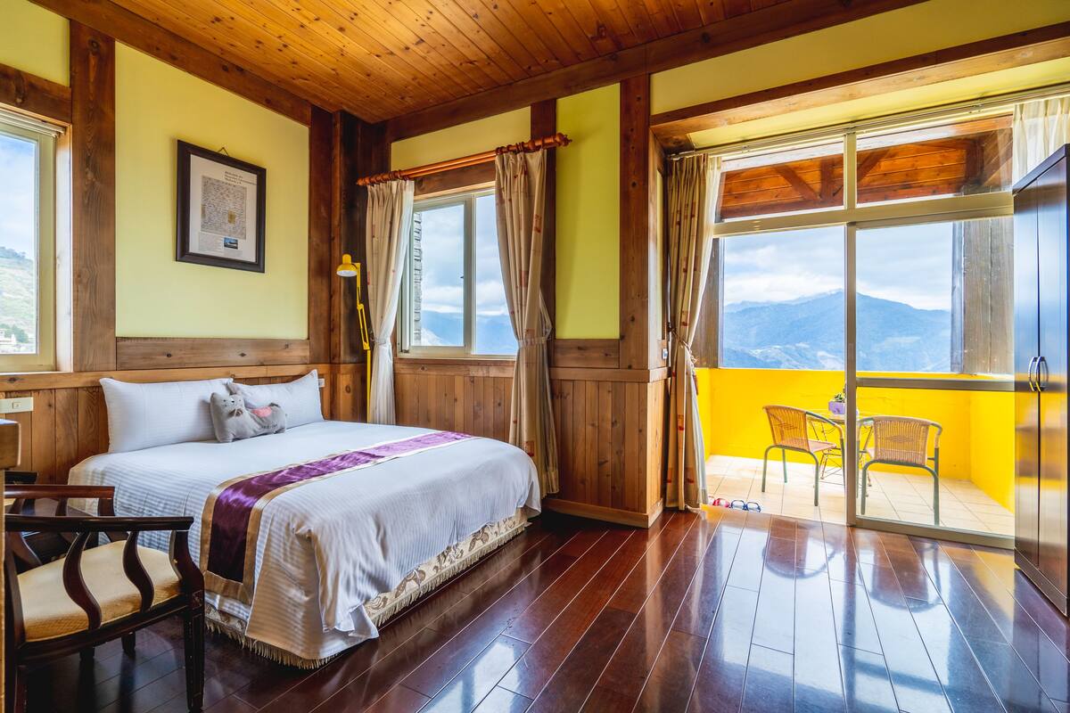Un dormitorio con cama, paredes de madera, una ventana y un balcón con sillas.