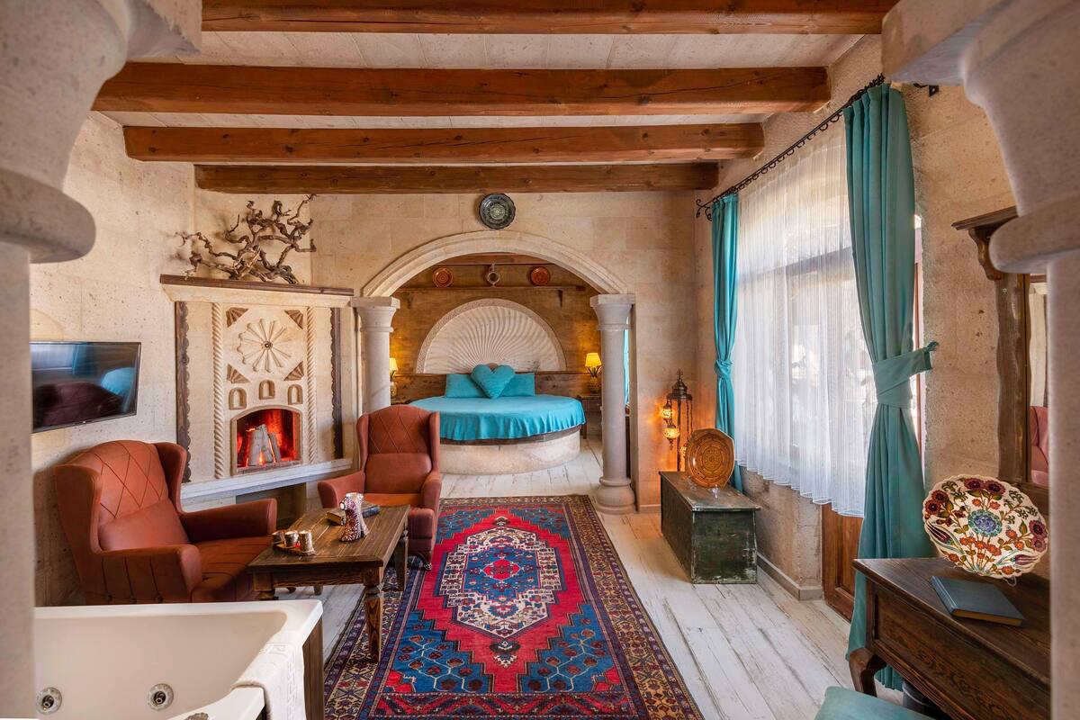 A cozy room with a bed, a fireplace, a wooden ceiling, and a patterned rug.