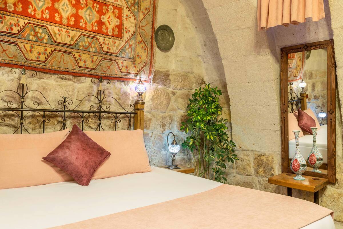 A bedroom with a bed, a nightstand, a mirror, and a wall with a patterned tapestry.