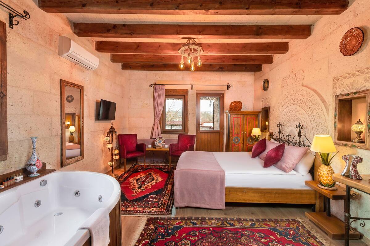 A cozy room with a large bed, a sitting area with chairs, a bathtub, and a television.