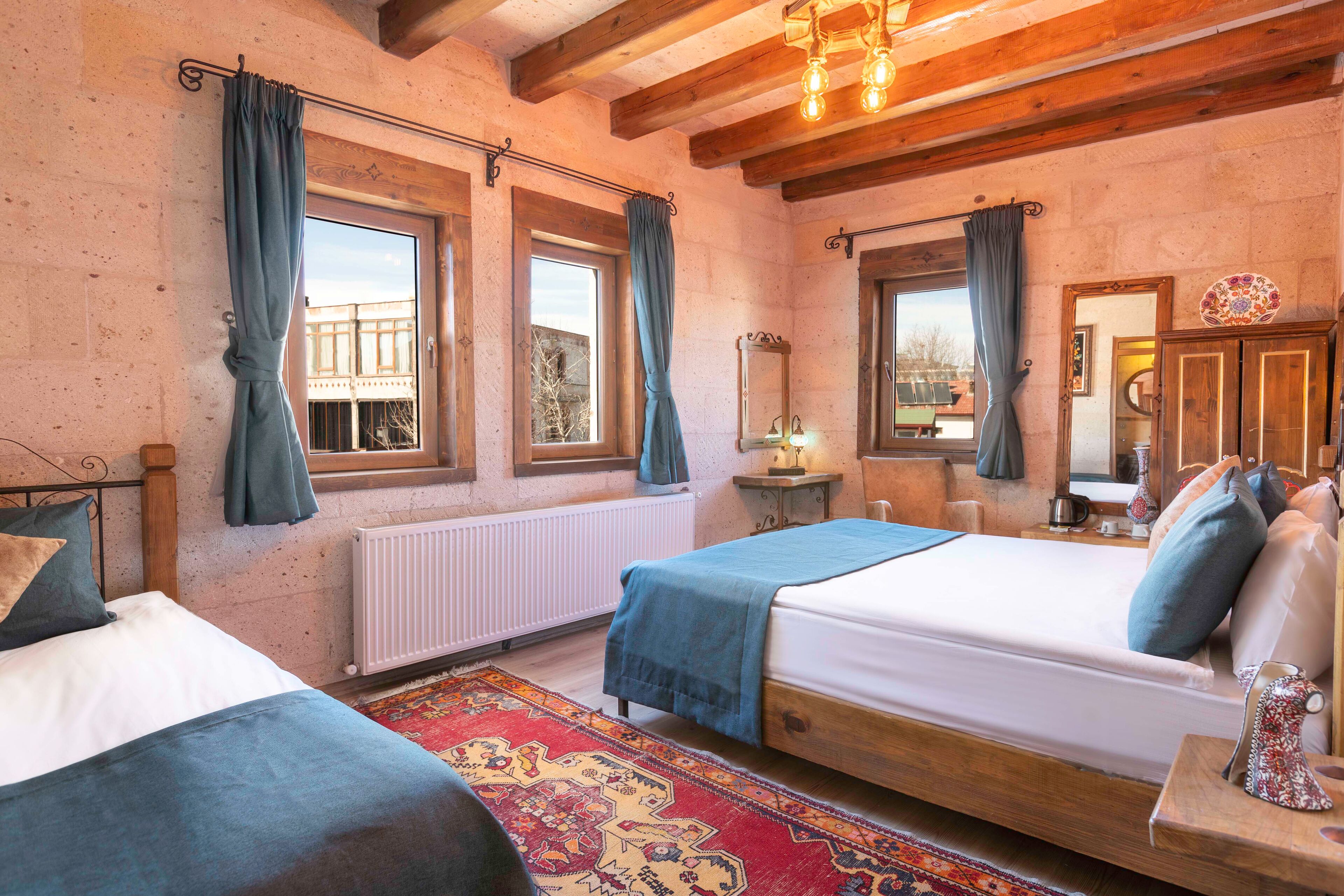 A bedroom with two beds, a large window, a radiator, and a wooden ceiling.