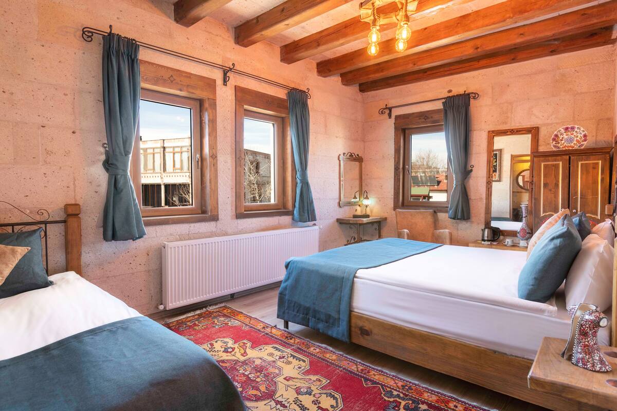 A bedroom with two beds, a large window, a radiator, and a wooden ceiling.