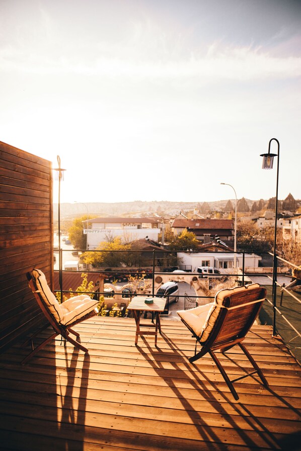 A wooden deck with two lounge chairs and a table, overlooking a residential area with houses and a hill in the background. - Maron Stone House (Nevsehir)