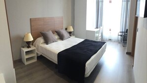 Una habitación de hotel con una cama grande, dos mesitas de noche, una silla y un escritorio.