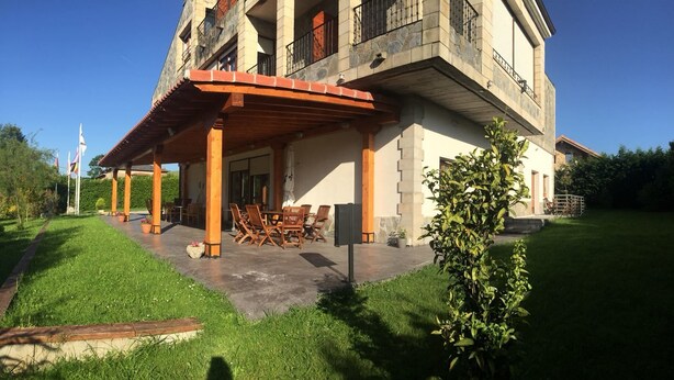 Un edificio de dos pisos con un patio cubierto, asientos exteriores y una bandera al fondo.
