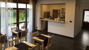 Un comedor con mesas y sillas de madera, una encimera con utensilios de cocina y vistas a zonas verdes.