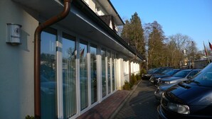 A row of parked cars in front of a building with large windows and a visible sign that reads "Warsteiner". - Schlosspark-Hotel Hof von Oldenburg (Rastede)