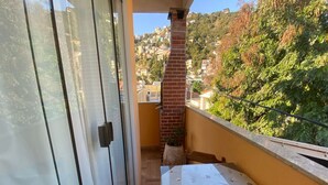 Un balcón con puerta de vidrio, chimenea de ladrillo y una mesa con mantel decorado con motivos de café.