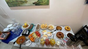 Una mesa de buffet con diversos alimentos y bebidas, incluyendo frutas, pasteles y un cuadro en la pared.