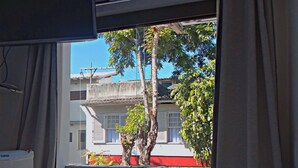 Una habitación con ventana que da a un balcón con un árbol y una cerca roja.