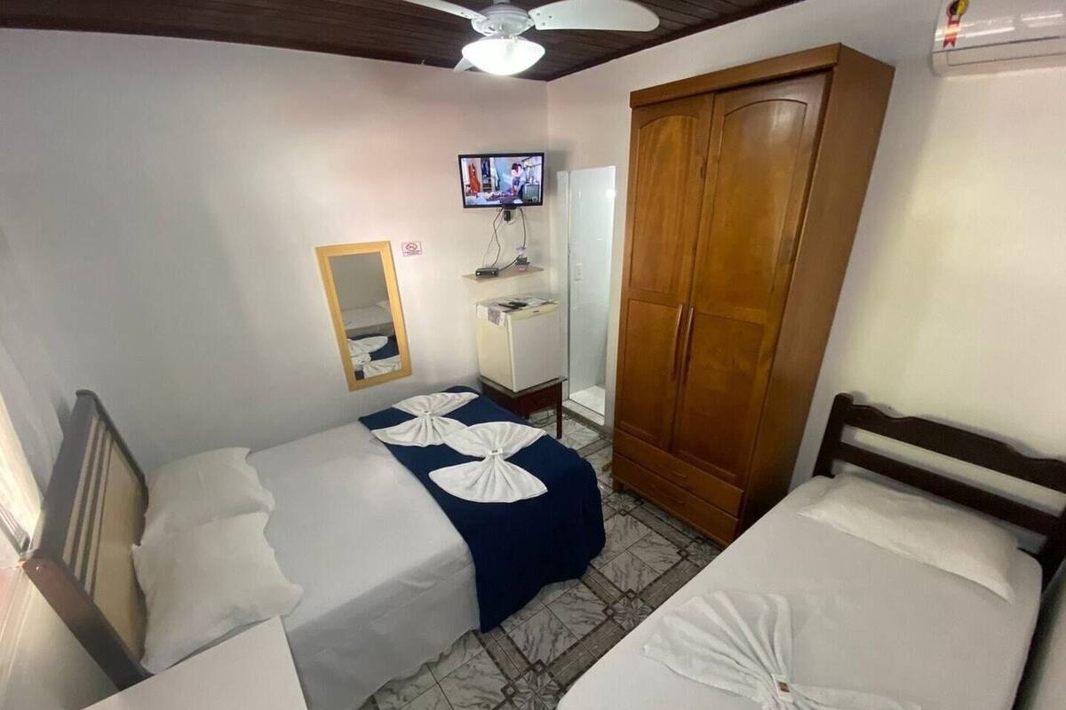 A hotel room with two beds, a wardrobe, a vanity with a mirror, a television on the wall, and a ceiling fan.