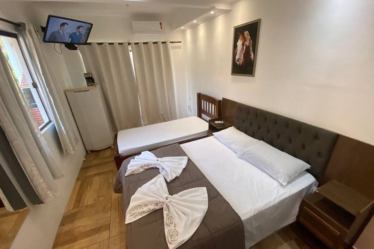 A hotel room with a bed, a bench, a TV, and a window with curtains.
