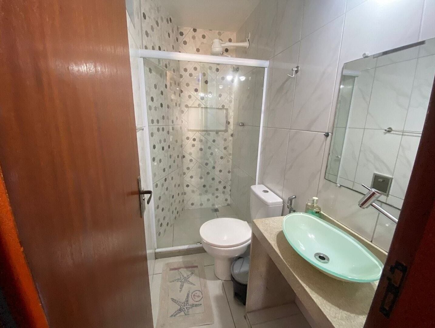 Ein Badezimmer mit Duschkabine aus Glas, Toilette und Waschbecken mit Spiegel.