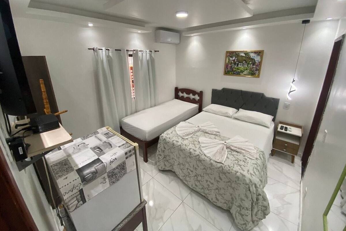 A hotel room with a single bed, a small desk with a computer, a chair, a window with curtains, and a painting on the wall.