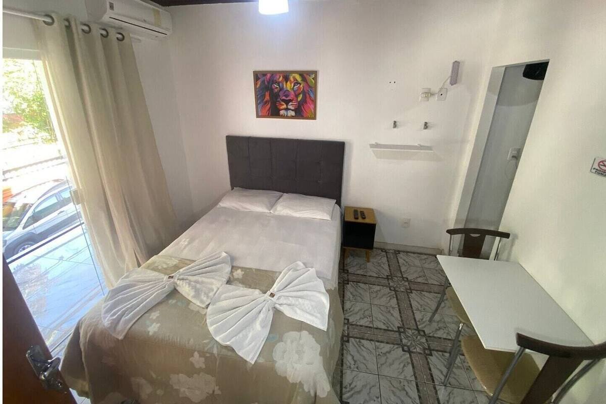 A hotel room with a bed, a desk, a chair, a painting on the wall, and a window with curtains.