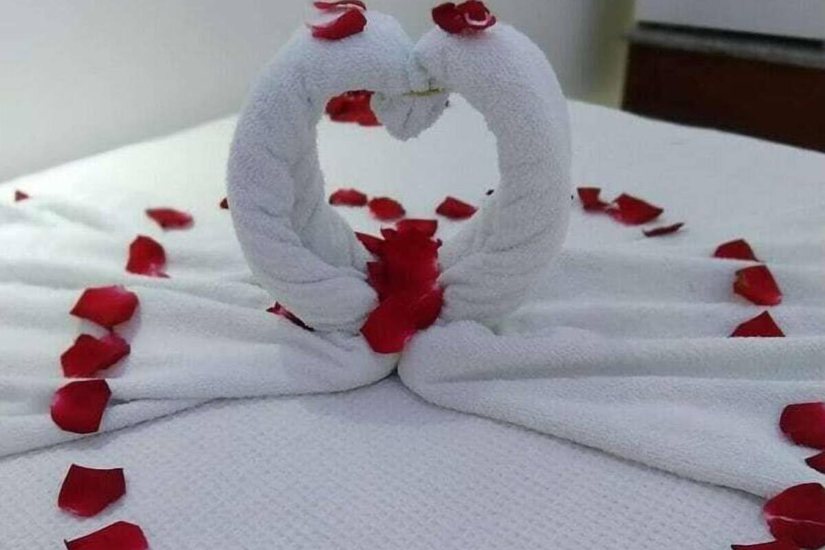 A towel with a heart shape made from rose petals and two towels forming a heart shape with red rose petals in the center.
