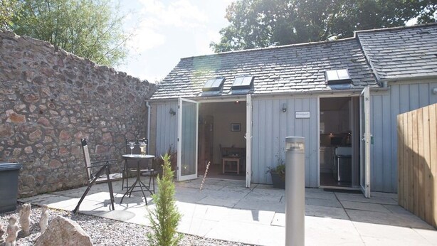 A covered outdoor area with a stone wall, a small table, chairs, and a potted plant.