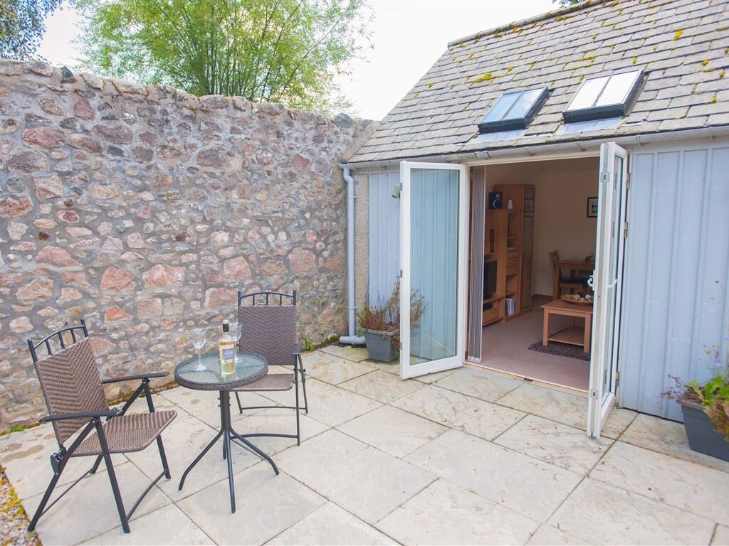 A stone wall, a patio with a table and chairs, and a room with a door open to the patio.