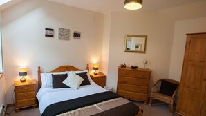 A bedroom with a bed, bedside tables, a dresser, a chair, a wardrobe, a mirror, and wall art.