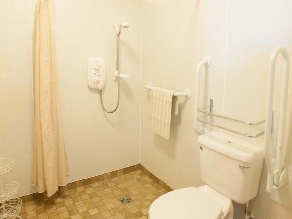 A small, clean bathroom with a toilet, shower, and handrails. - Glenernan Self Catering Cottages (Ballater)