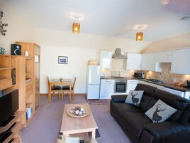 Un espacio habitable compacto con kitchenette, comedor y zona de estar con sofá y televisor.