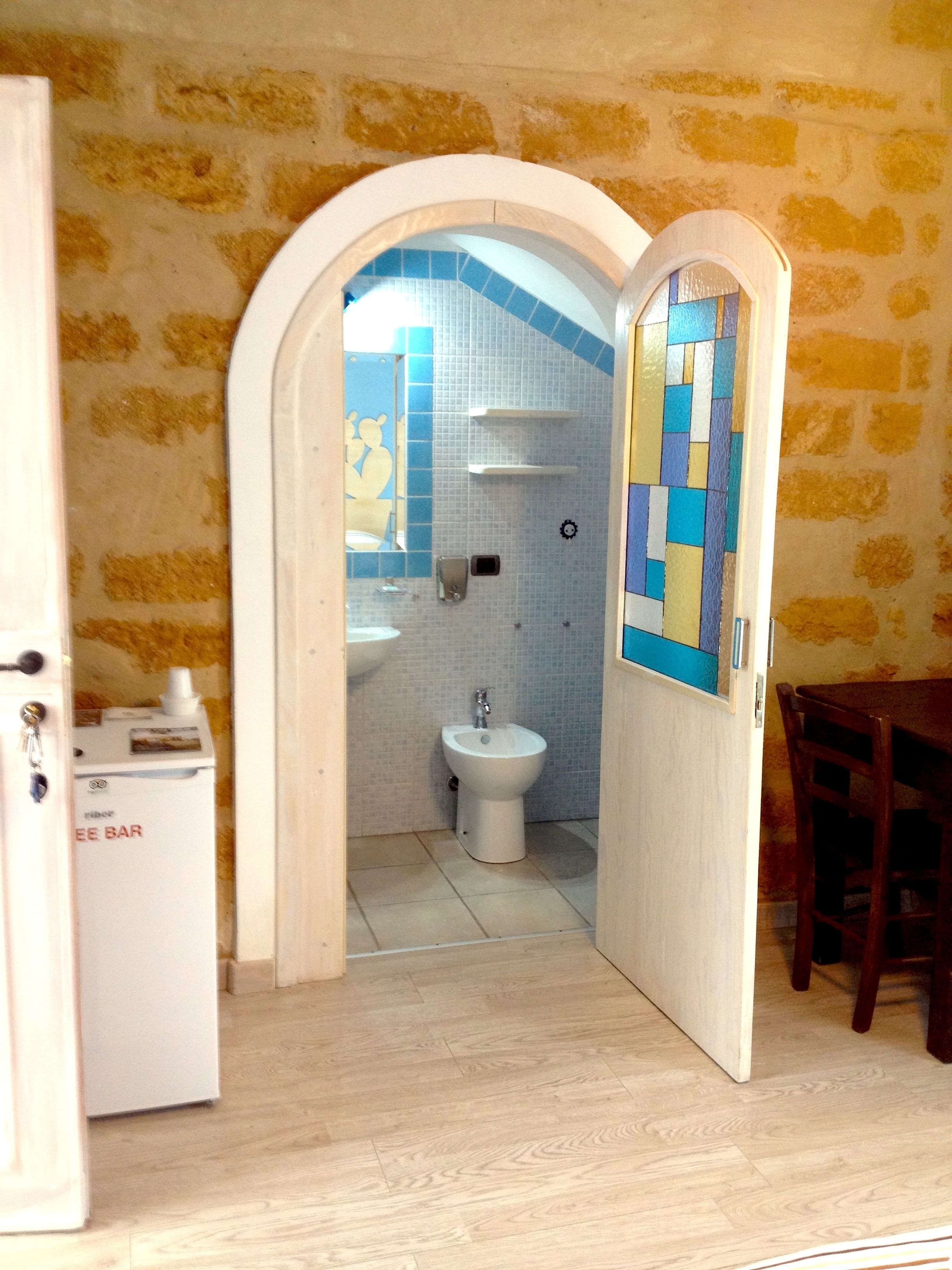 Un pasillo estrecho que conduce a un baño con inodoro, lavabo y un refrigerador pequeño.