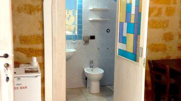 Un pasillo estrecho que conduce a un baño con inodoro, lavabo y un refrigerador pequeño.