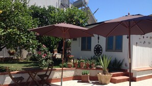 An outdoor patio with two brown umbrellas, a wooden chair, and various potted plants. - B&B San Leone (Agrigento)