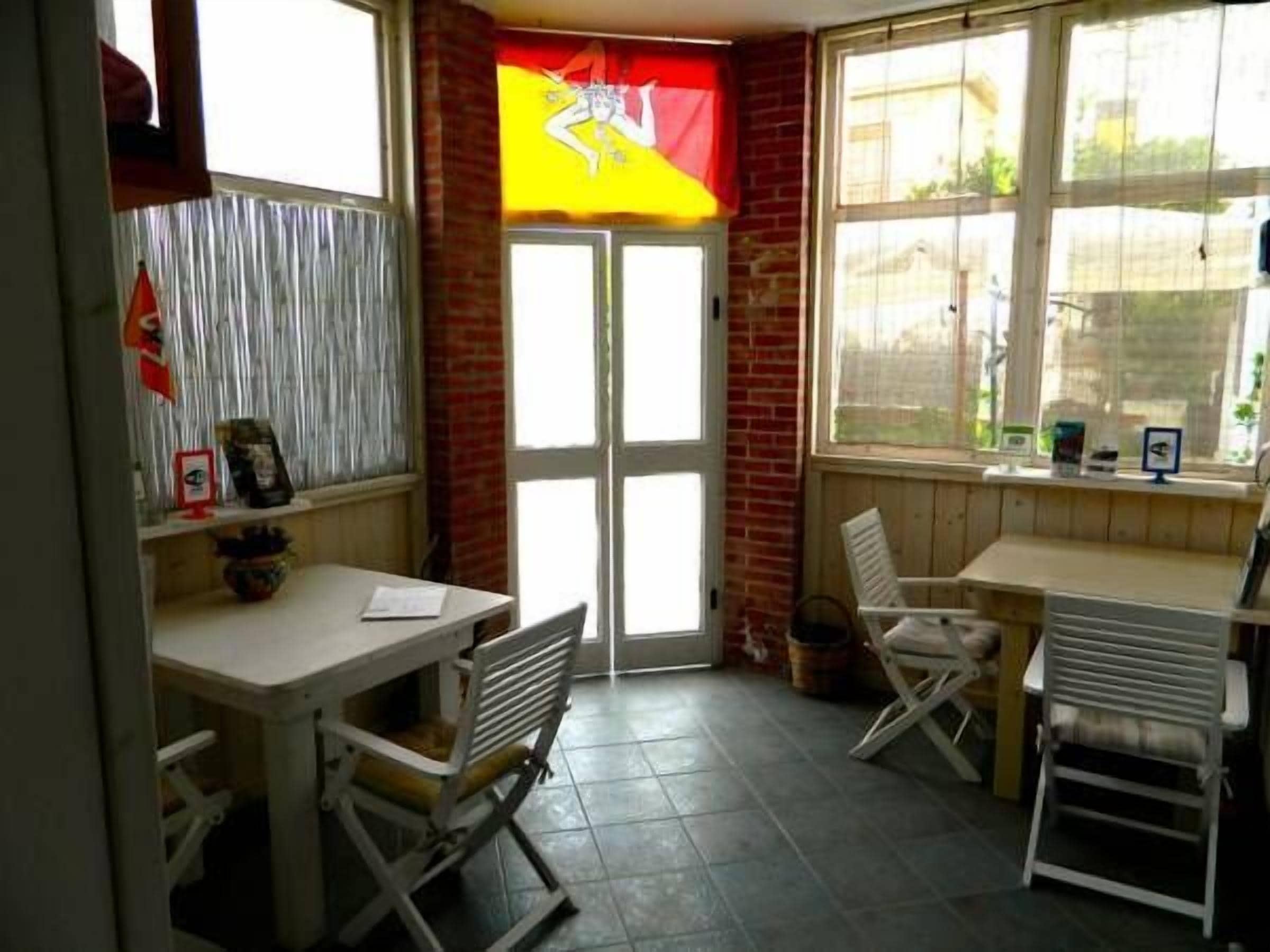 A small, bright room with a tiled floor, a white table, two white chairs, and a window with a view of the outside.