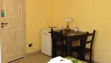 Una habitación con cama, escritorio, silla, un refrigerador pequeño y una puerta.