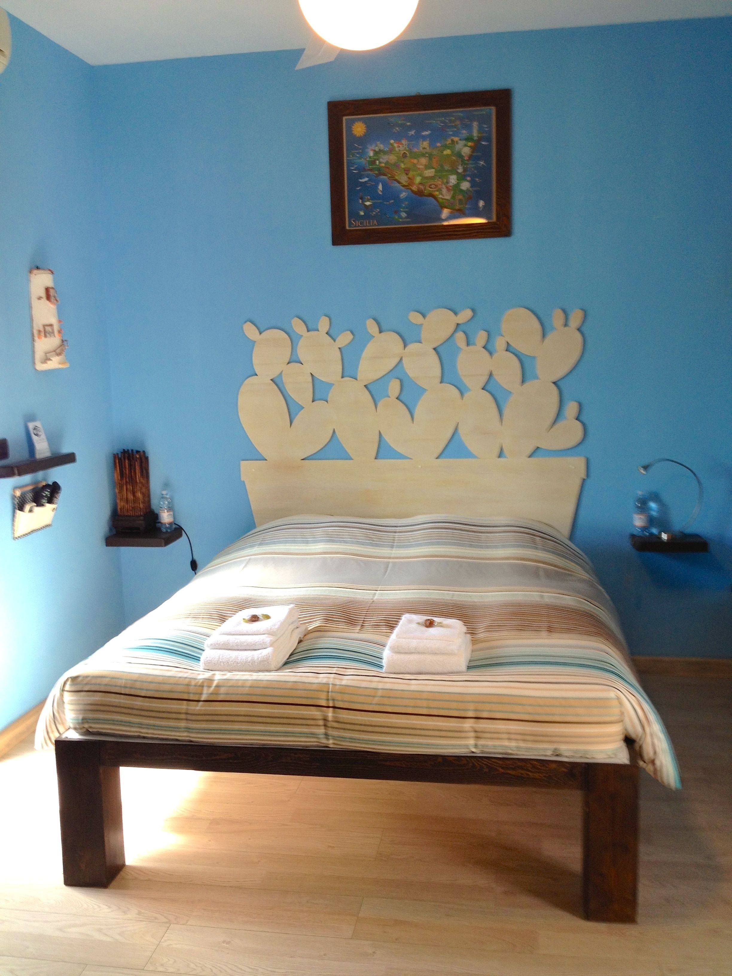 Une chambre à coucher avec un lit, des murs bleus, une tête de lit en forme de cactus et une carte de la Sicile accrochée au mur.