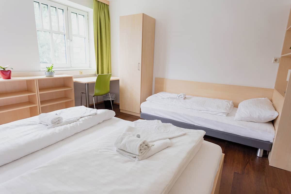 A hotel room with two beds, a desk, a chair, and a wardrobe.