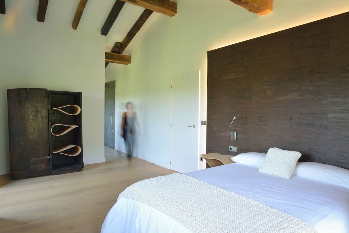 A modern bedroom with a large bed, wooden beams, a dark wooden wardrobe, and a white door.
