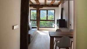 A room with a wooden ceiling, a sofa, a TV, and a dining area with chairs. - Arantza Apartamentuak (Arantza)