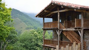 A wooden cabin with a balcony, stone foundation, and a view of a forested mountain range. - Arantza Apartamentuak (Arantza)
