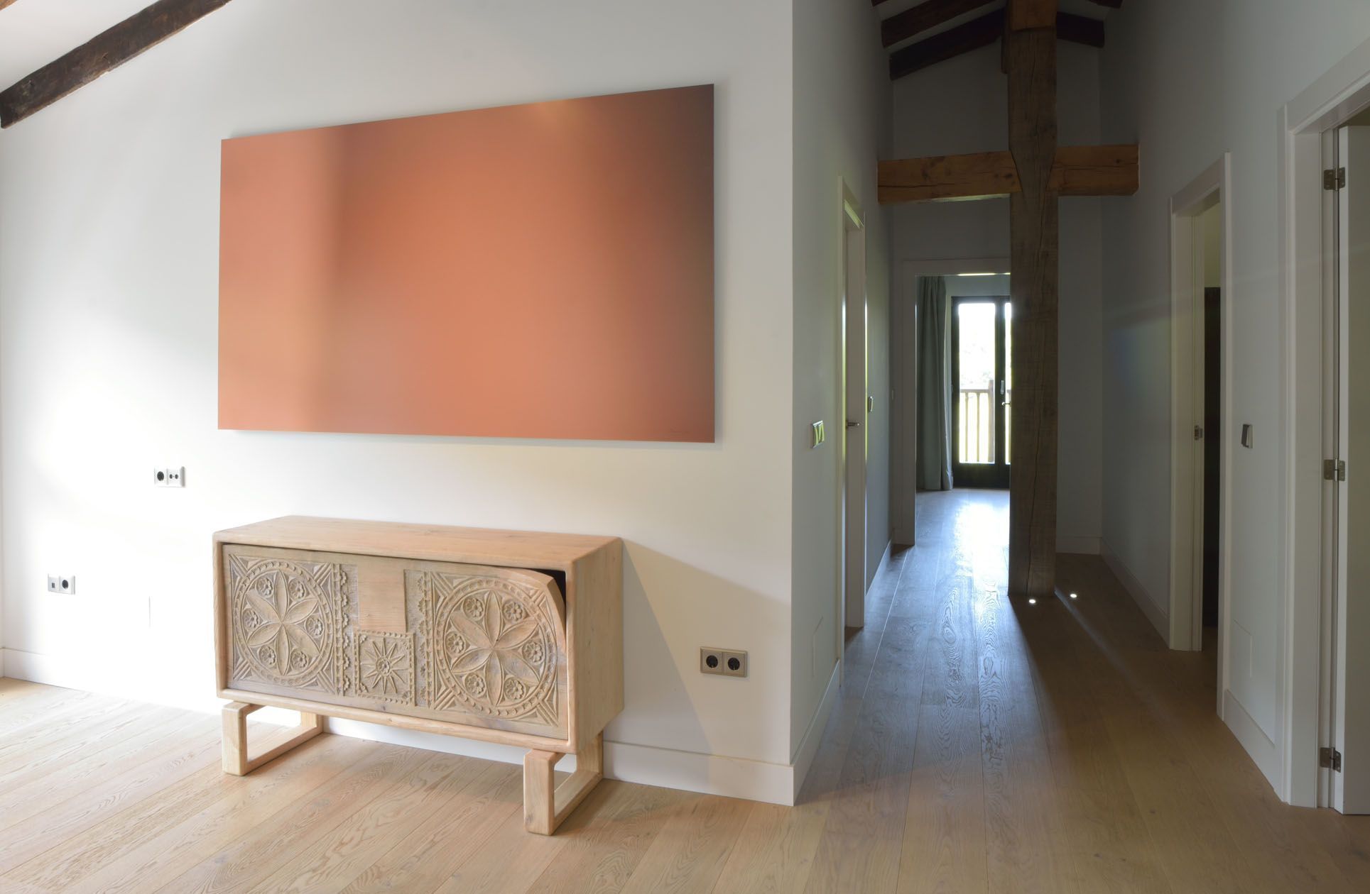 Un pasillo con un armario de madera, una obra de arte naranja grande y una puerta que da a otra habitación.